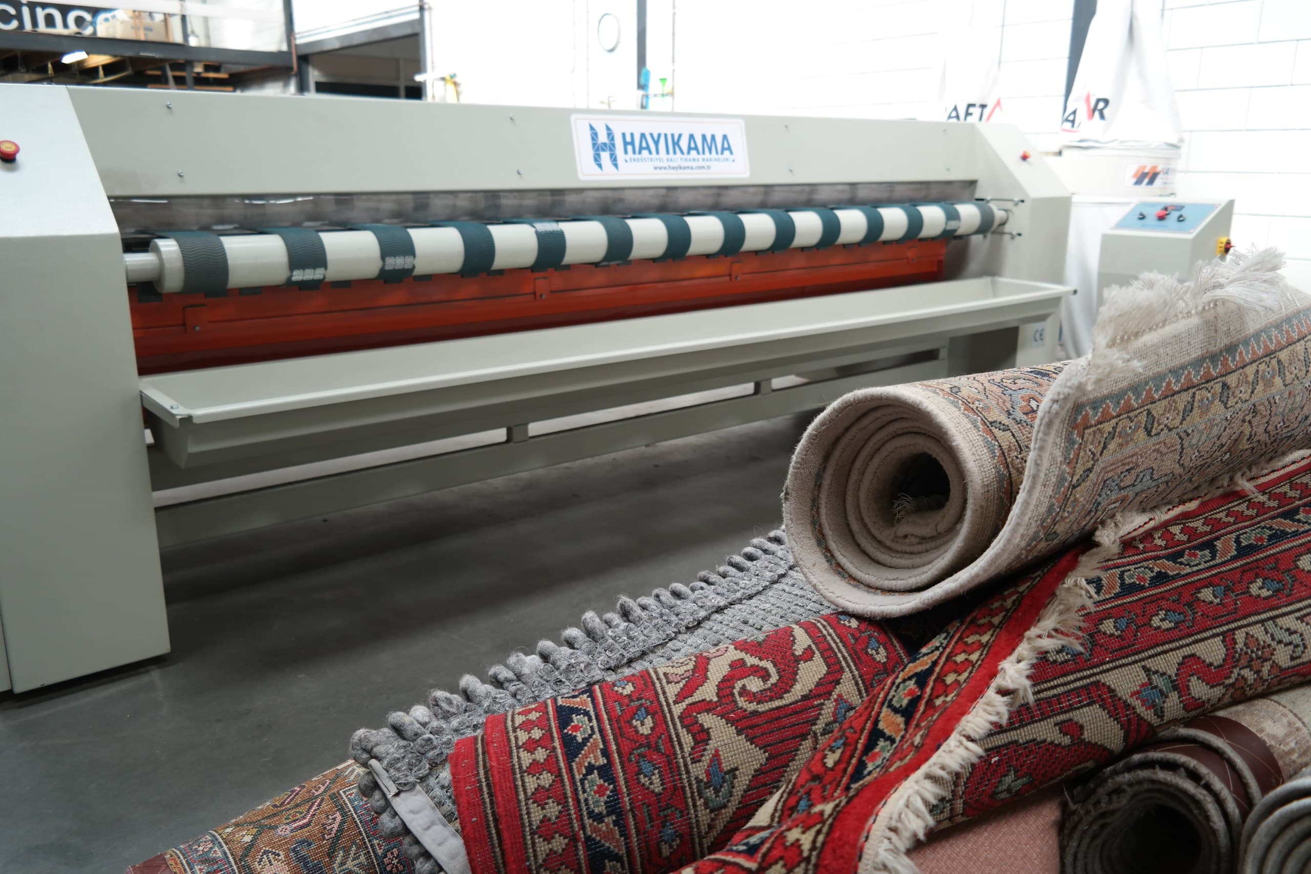 Opgerolde Perzische vloerkleden voor een industriele tapijtwasmachine in de wasserij