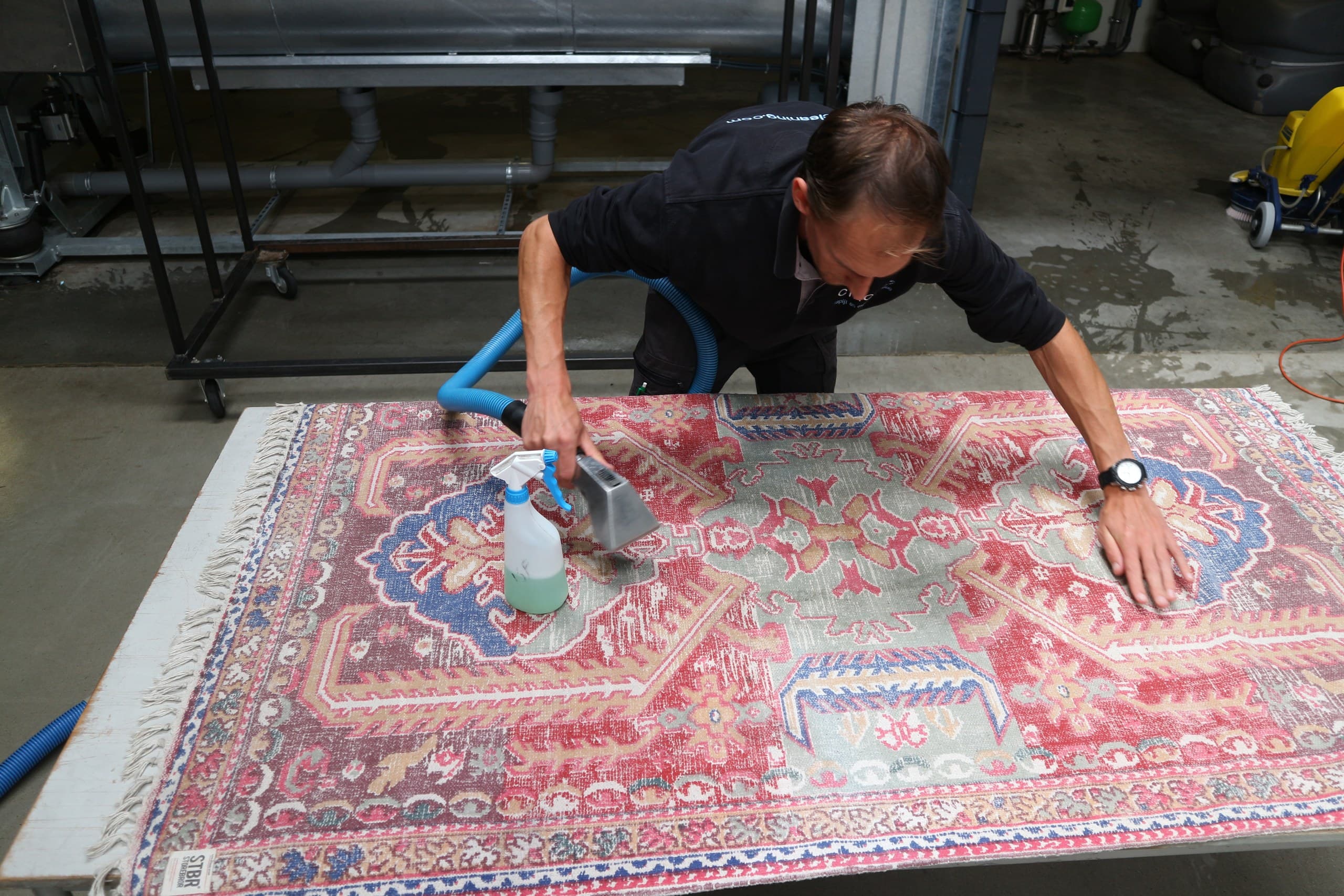 Medewerker behandelt een vlek op een Perzisch vloerkleed met sproeier en zuigmond